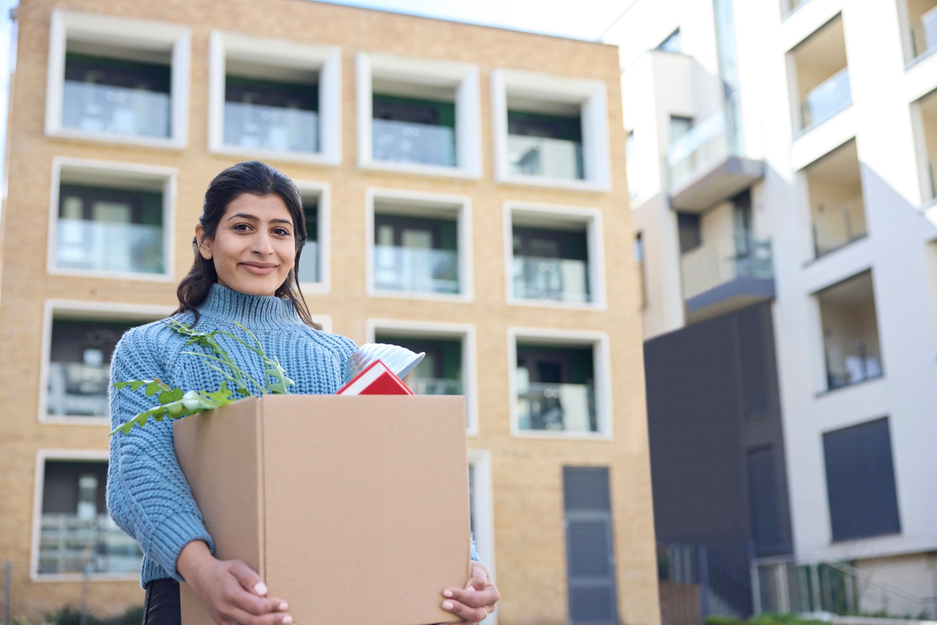 Portrait Of Female University Or College Student Outdoors Moving Into Campus Room Carrying Box