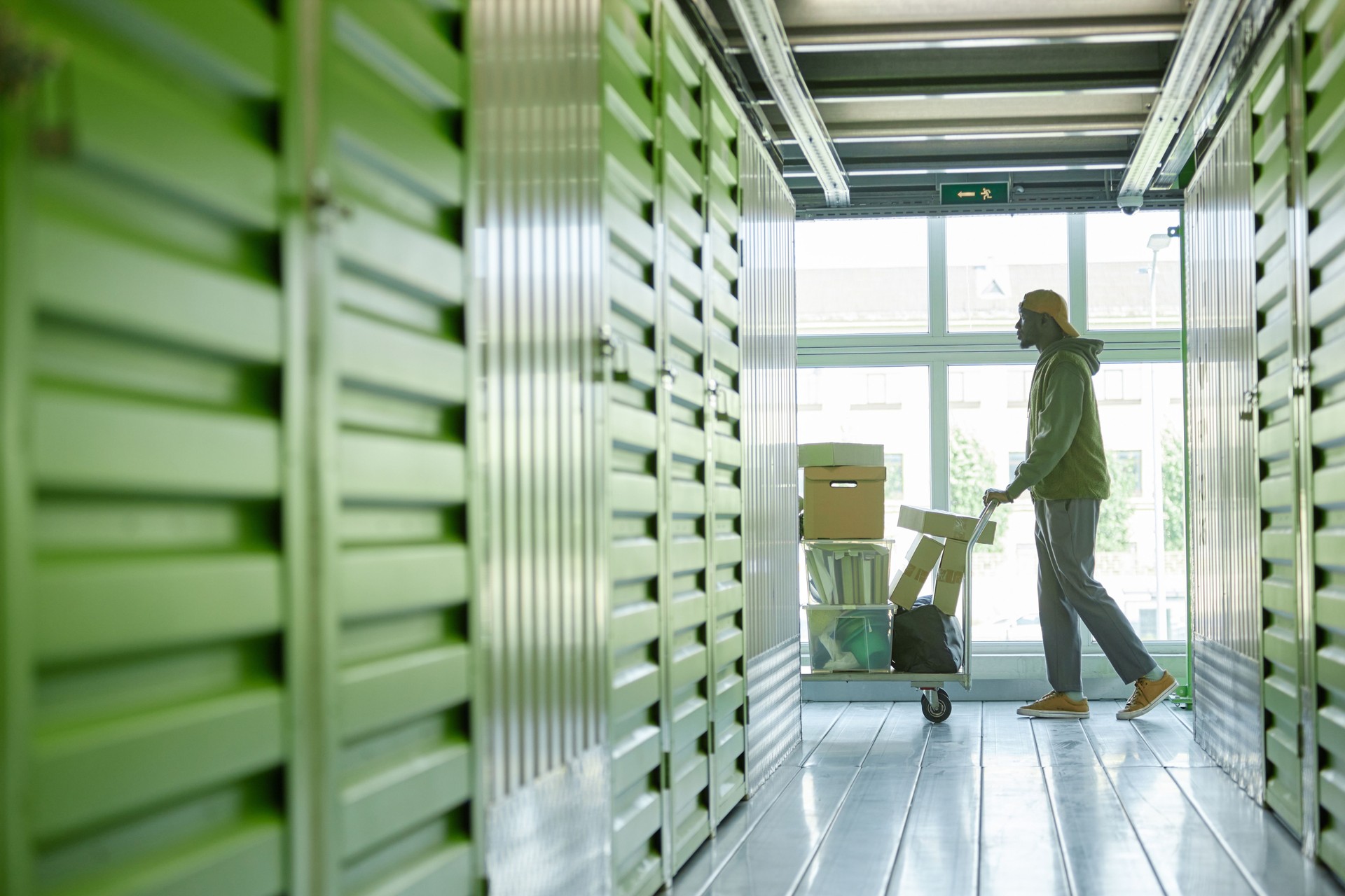 Black Man Transporting Boxes on Cart into Self Storage Unit at Warehouse while Moving out
